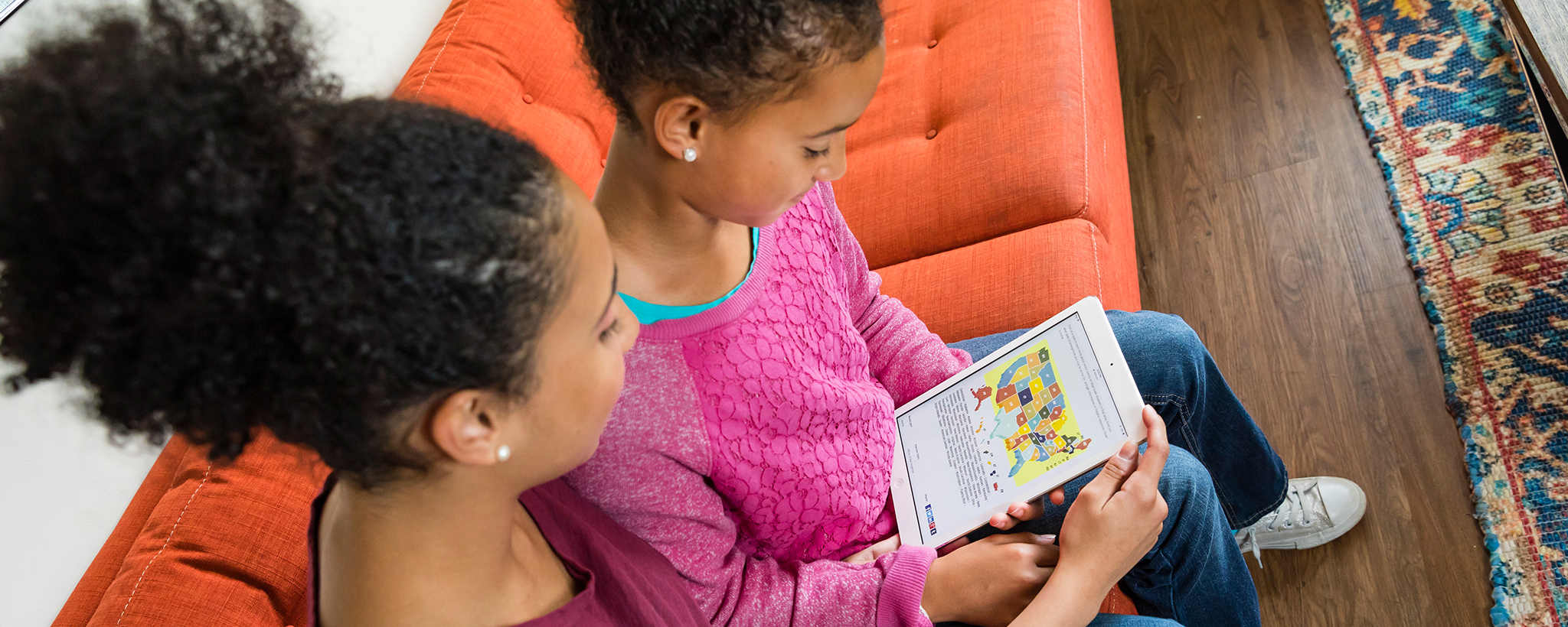 An older girl and a child are using a tablet devices to examine a map of the United States