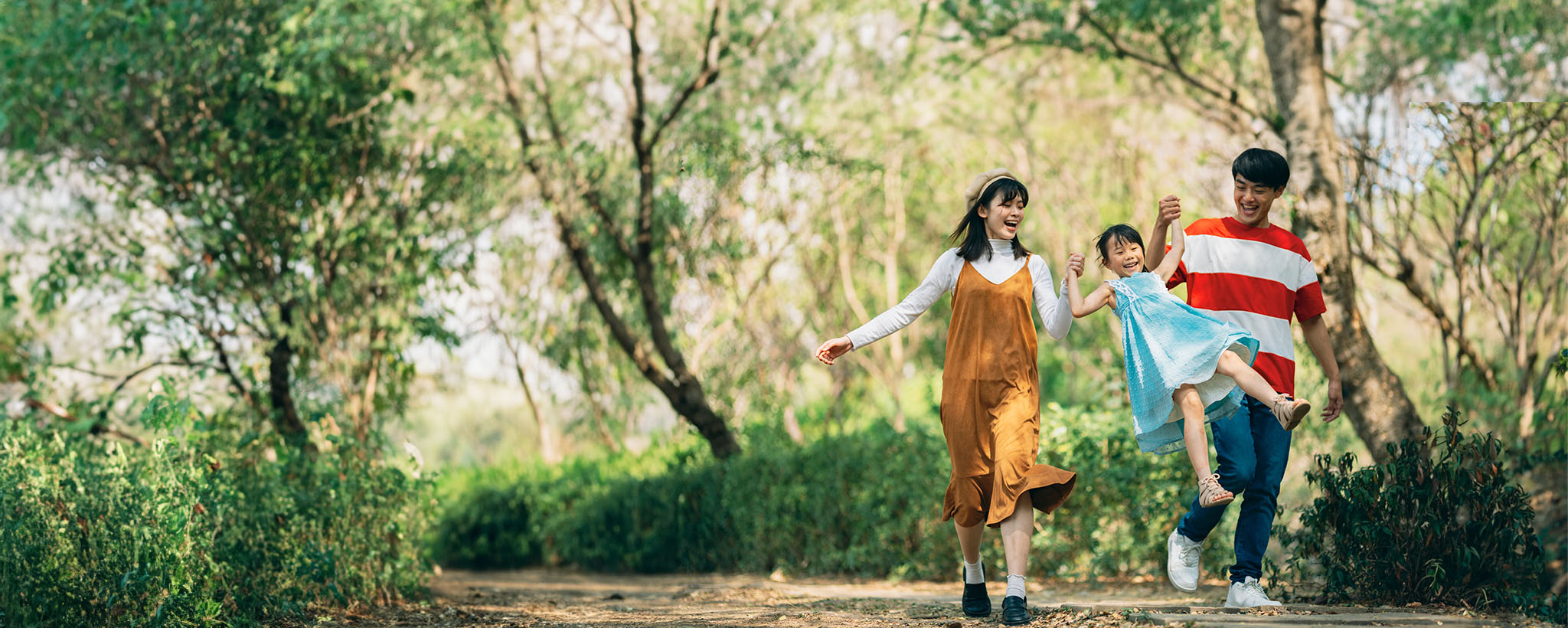 A family of Asian descent walks on a path together, mother, father and young daughter. 