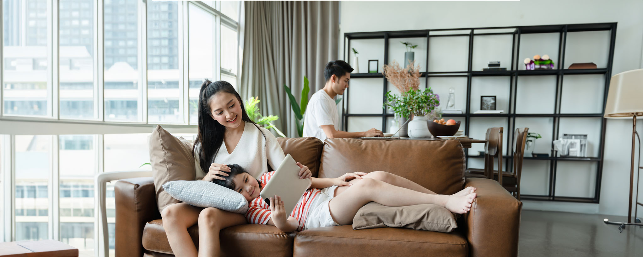 Una familia asiático-americana sentada en su sala de estar, la hija mira una tableta.