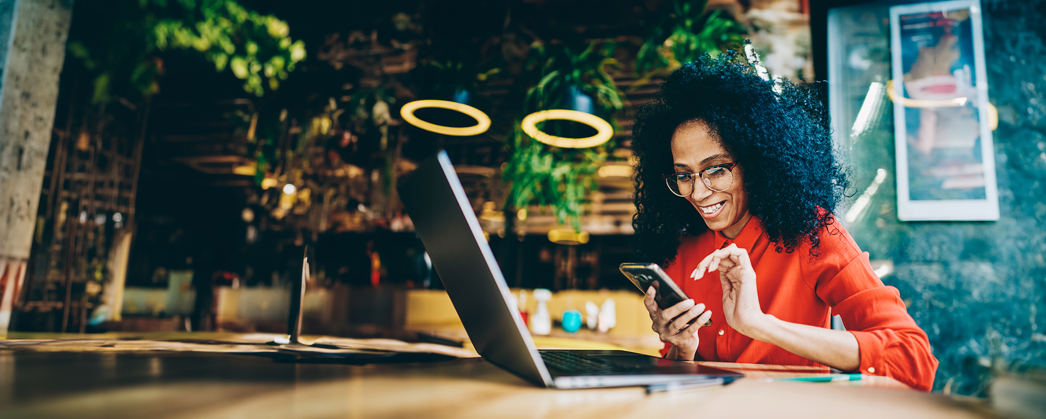 A woman works on her laptop and looks at her phone. 