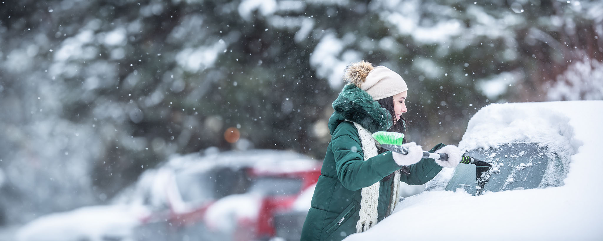 A woman in the snow clearing snow off her car windshield. 