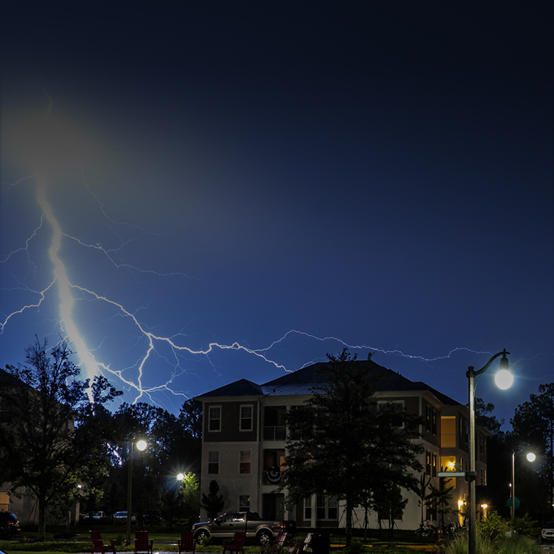 Image shows a lightning bolt striking in the background of an apartment building.