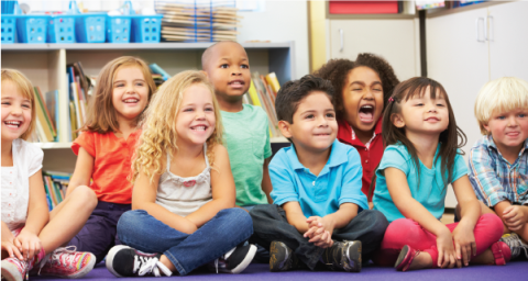 A group of young school children sit on a classroom floor