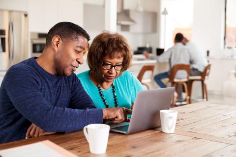 A middle aged son showing his older mother how to make a plan on a laptop. 